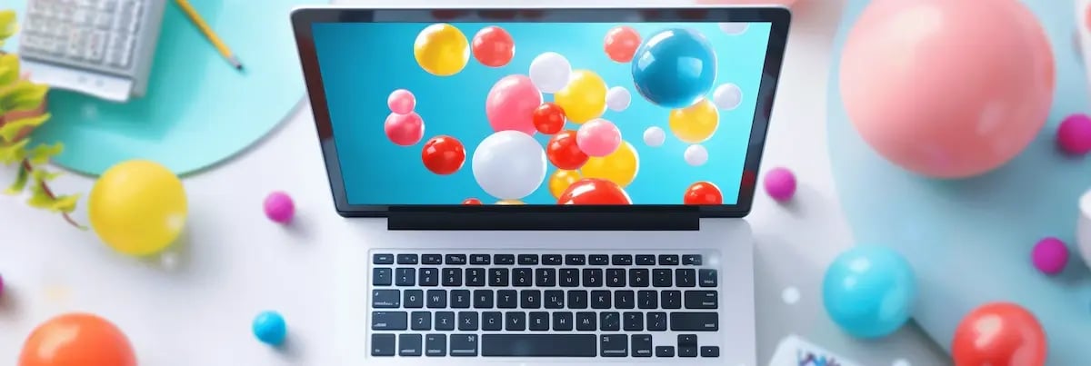a laptop on a table. on the laptop screen are balloons, and surrounding the laptop on the table are also balloons.