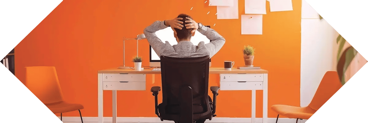 man with hands on head in orange office in front of computer
