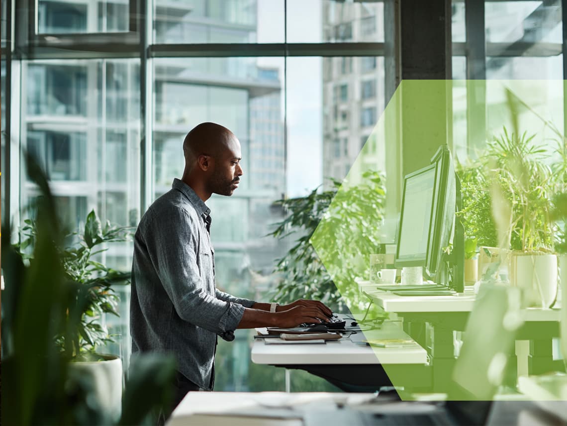 a person typing on a computer inside an office. They are surrounded by green plants.